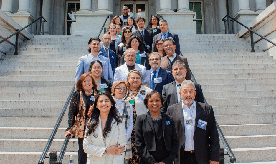 Smiling Latino people lining the steps as a group outside of a government building